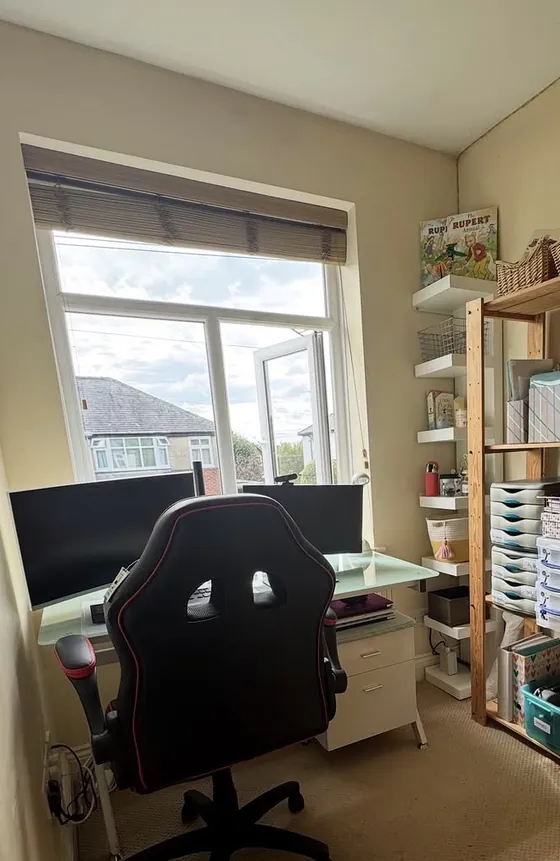 The same office after: the desk moved to the window with a clear top, open shelving with labelled boxes, and a clear floor